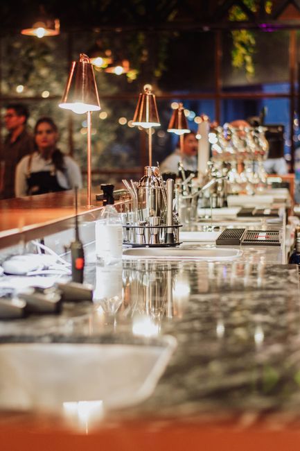 Close-up of a polished stainless steel beer tap system in a pub or restaurant setting, featuring multiple taps and a round tap handle with the brand name 'Sperbermann' visible. The surface of the taps