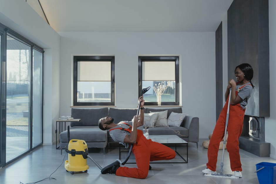A team of three professional cleaners performing a deep, surface cleaning in a modern, bright kitchen. The scene shows a stainless steel oven built into a white marble-like wall with modern cabinetry.